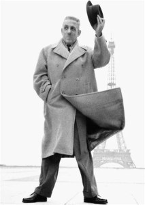 Photograph of Francis Poulenc in a coat in the breeze before the Eiffel Tower